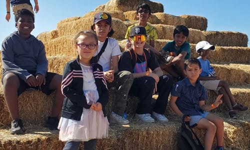 Group of kids sitting on stacked hay bales